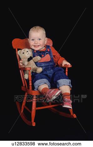 Stock Photo - Toddler sitting in red rocking chair with teddy bear. Fotosearch