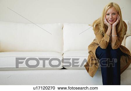 Stock Image - Woman sits on sofa. Fotosearch