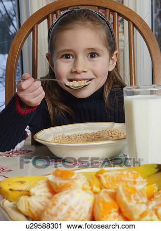 Stock Image - Young girl eating cereal at breakfast table. Fotosearch