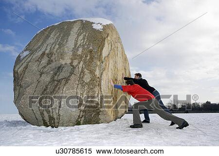 Stock Photography - 2 men pushing massive boulder. Fotosearch