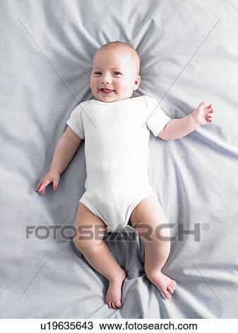 Stock Image - Baby girl on bed, shot from above. Fotosearch