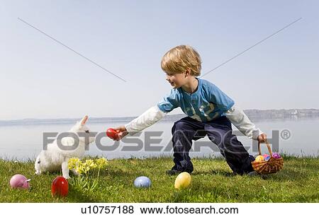 Stock Photo - boy, bunny finding easter eggs. Fotosearch