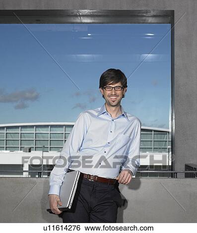 Businessman smiling, holding laptop View Large Photo Image Stock Photograph - Businessman smiling, holding laptop. Fotosearch