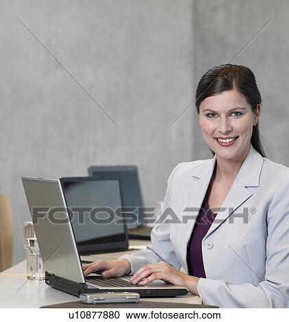 Stock Image - Businesswoman using laptop, smiling. Fotosearch