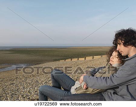 Stock Photo - Couple cuddling on pebbled beach. Fotosearch