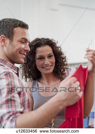 Stock Photograph - couple shopping holding up red dress. Fotosearch
