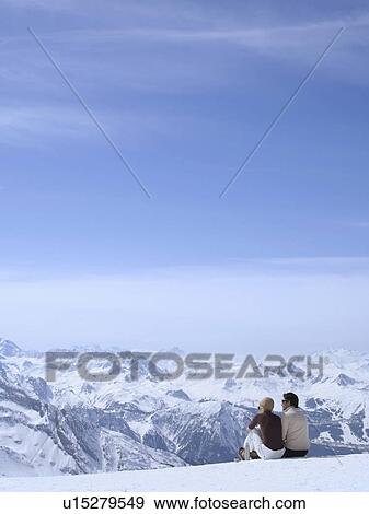 Stock Photo - couple sitting in the snow hugging. Fotosearch
