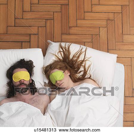 Stock Image - Couple sleeping, wearing eye-masks. Fotosearch