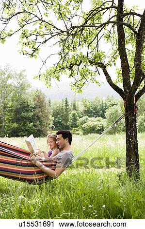 Stock Image - Father And Daughter Reading In Hammock. Fotosearch