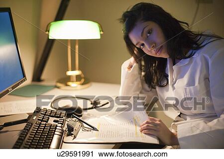 Stock Image - Female Doctor working at desk at night. Fotosearch