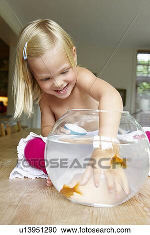 Stock Image - Girl trying to catch a fish, in a bowl. Fotosearch