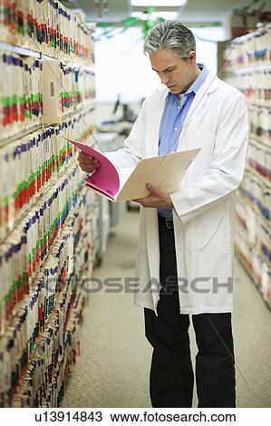 Stock Image - Male Doctor reading medical file. Fotosearch