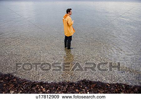 Stock Photo - man in raincoat in shallow water. Fotosearch
