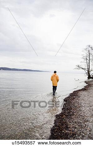 Stock Photo - man in raincoat wading along shore. Fotosearch