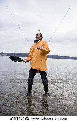Stock Image - man in raincoat with racket and ball. Fotosearch