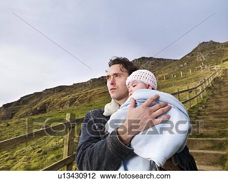 Stock Image - man on hill path holding baby. Fotosearch