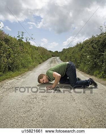 Stock Image - Man With Ear Pressed to Road Surface. Fotosearch