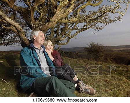 Stock Image - mature couple sitting against tree. Fotosearch