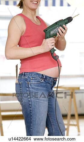 Picture - pregnant woman with power drill. Fotosearch