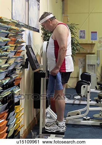 Stock Image - senior man on scales at gym. Fotosearch