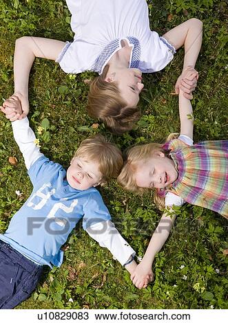 Stock Image - two girls and boy lying in grass. Fotosearch