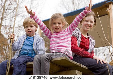 Stock Photograph - two girls and boy sitting in tree house. Fotosearch
