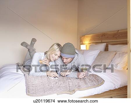 Picture - woman and man lying on bed eating. Fotosearch