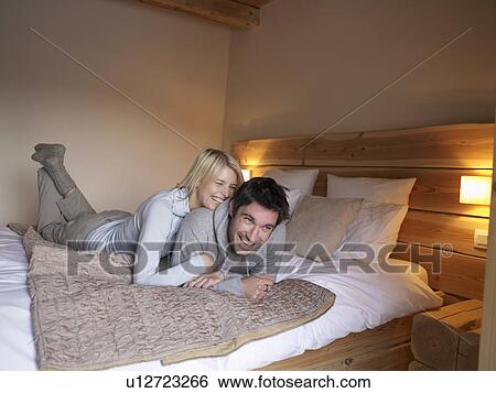 Stock Photograph - woman and man lying on bed playing. Fotosearch