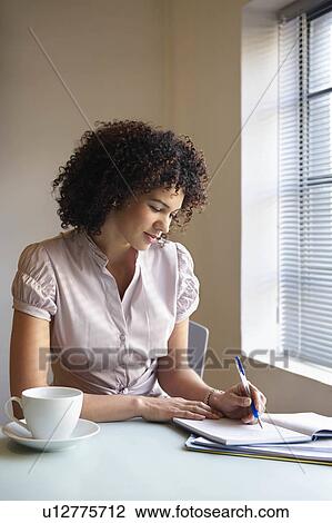 Woman by window writing in a book View Large Photo Image Stock Image - Woman by window writing in a book. Fotosearch