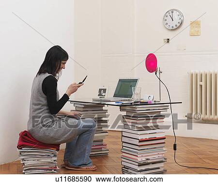 Woman sitting at desk, holding phone View Large Photo Image Stock Image - Woman sitting at desk, holding phone. Fotosearch