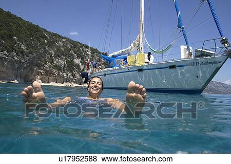 Stock Photo - Woman Swimming next to moored boat. Fotosearch