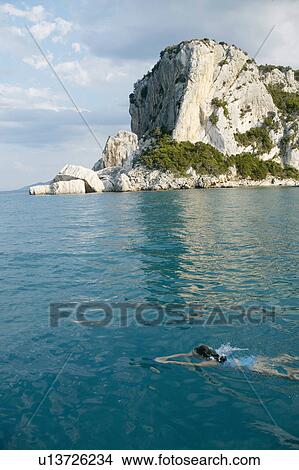 Picture - Woman swimming off rocky coastline. Fotosearch