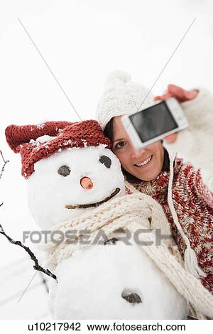 Stock Image - woman taking photo of snowman. Fotosearch