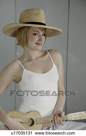 Stock Image - Woman wearing hat playing toy guitar.. Fotosearch