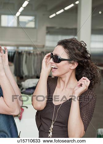 Stock Image - women shopping trying on sunglasses. Fotosearch