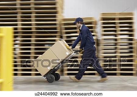 Stock Image - Worker pushing trolley in warehouse. Fotosearch