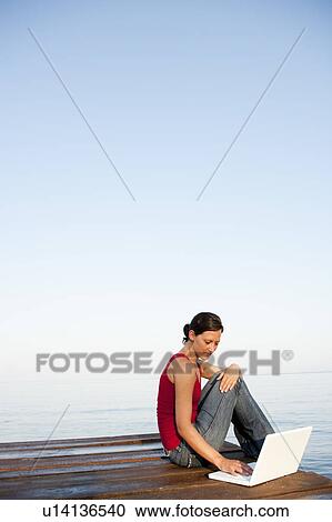 Stock Image - Young Woman On Jetty Looking At Laptop. Fotosearch