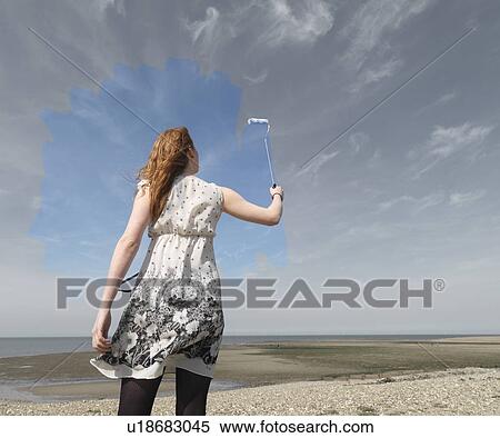 Stock Photography - Young woman painting grey sky blue. Fotosearch