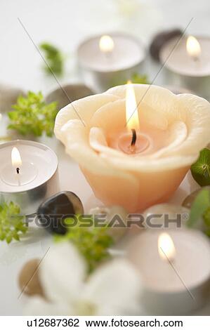 Stock Image - Burning candles and stones, close up, white background. Fotosearch