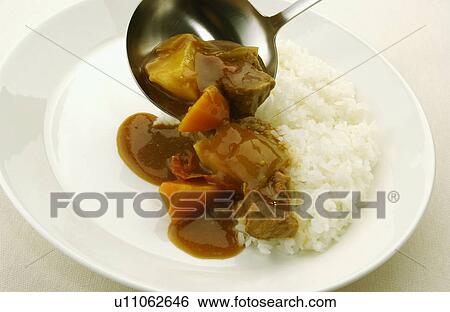 Stock Photograph - Curry being poured on plate of rice, white background. Fotosearch