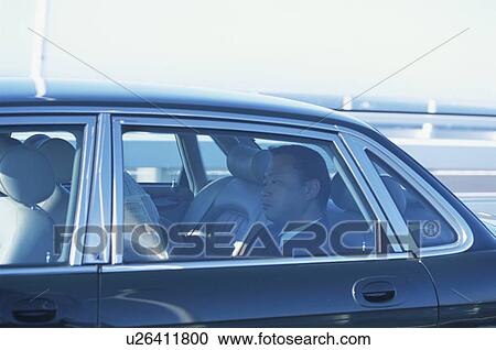 Stock Image - Mature businessman reading newspaper in car. Fotosearch