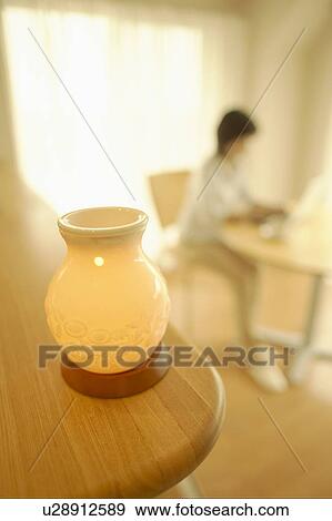 Stock Photo - Oil lamp, woman sitting at table in background, differential focus. Fotosearch