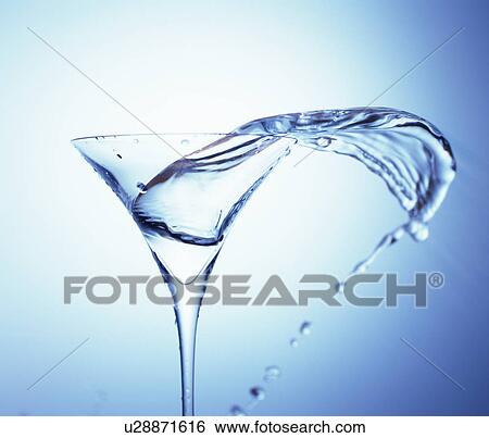 Stock Photograph - Water spread out from cocktail glass, blue background. Fotosearch
