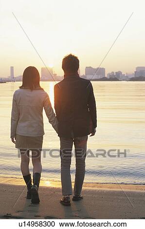 Stock Image - Young couple walking on beach, hand in hand. Fotosearch