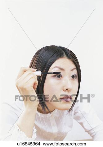 Picture - Young woman applying mascara, white background. Fotosearch