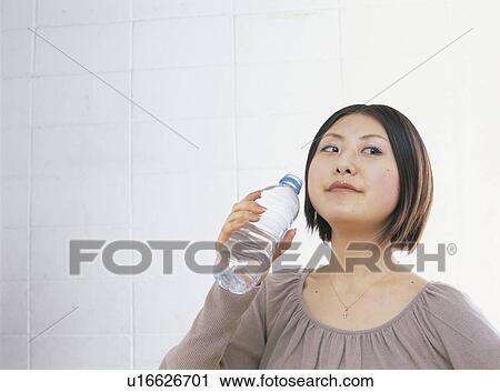 Stock Image - Young woman holding a bottle of water, looking away. Fotosearch