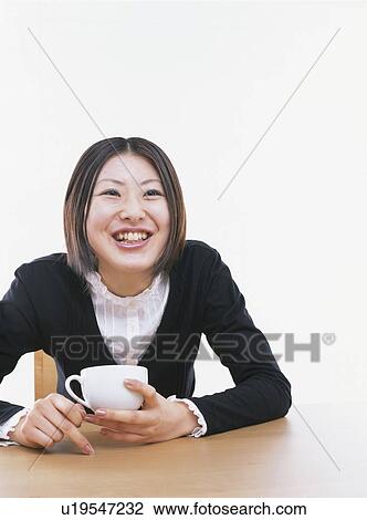 Stock Image - Young woman holding a coffee cup, smiling, white background. Fotosearch