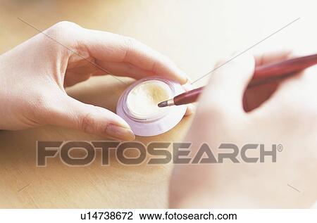 Stock Image - Young woman holding lipstick and brush, close up. Fotosearch