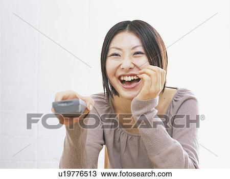 Young woman holding remote control, smiling, white background View Large Photo Image Stock Image - Young woman holding remote control, smiling, white background. Fotosearch