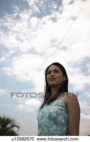 Young woman standing under blue sky, smiling and looking away View Large Photo Image Stock Image - Young woman standing under blue sky, smiling and looking away. Fotosearch